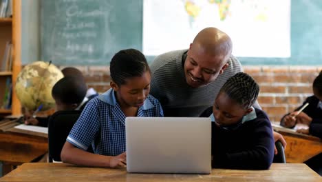 male teacher using laptop with student in classroom 4k