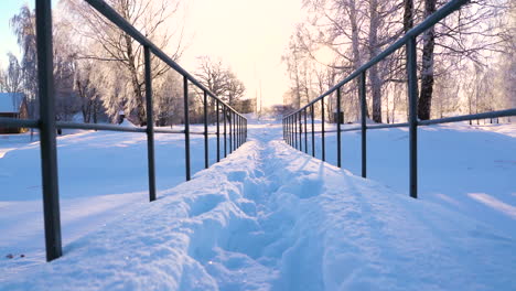 snow covered metal bridge ahead leads towards sunlight on cold winter morning