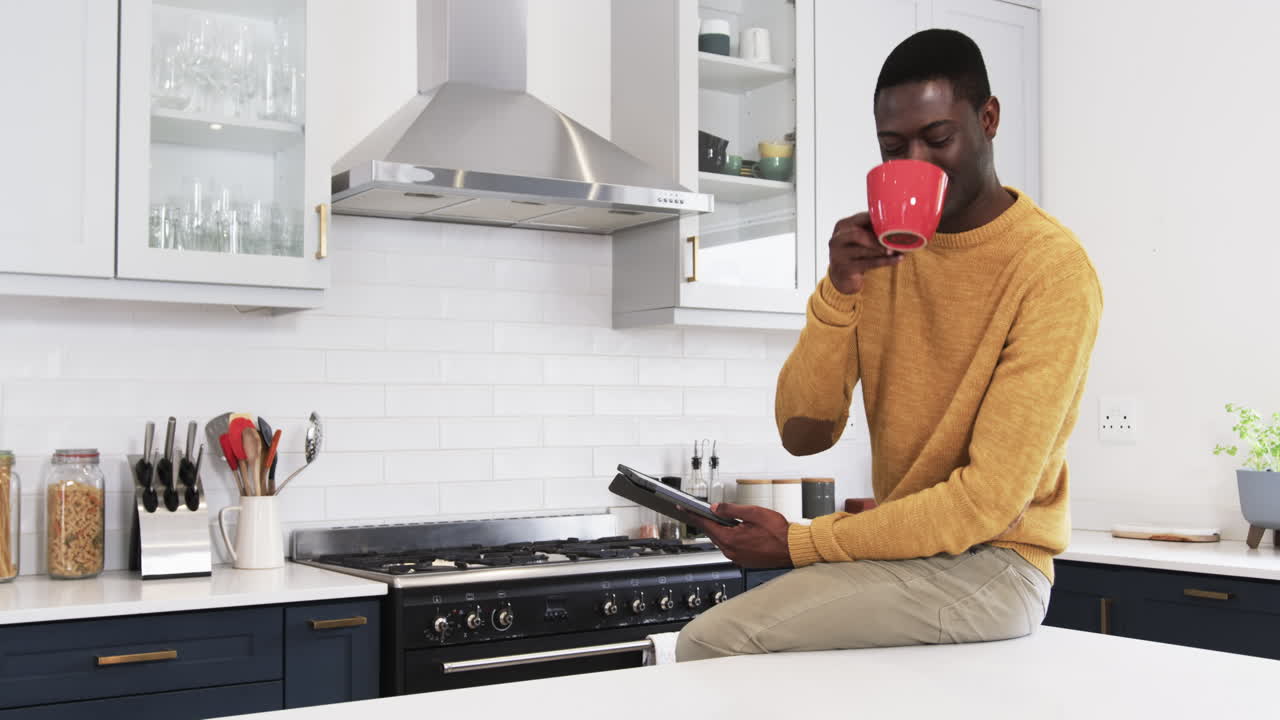 Uomo in cucina che beve caffè e legge il tablet, godendosi la routine mattutina, spazio per il testo.