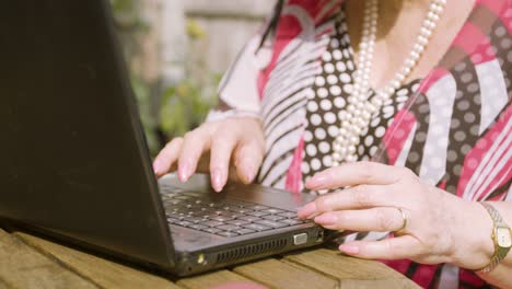 elderly woman close up on her hands typing on a black laptop outside