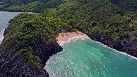 Playa-De-Arena-Escondida-Detrás-De-Una-Costa-Rocosa-Gigante-Con-Plantas-Verdes-En-Verano