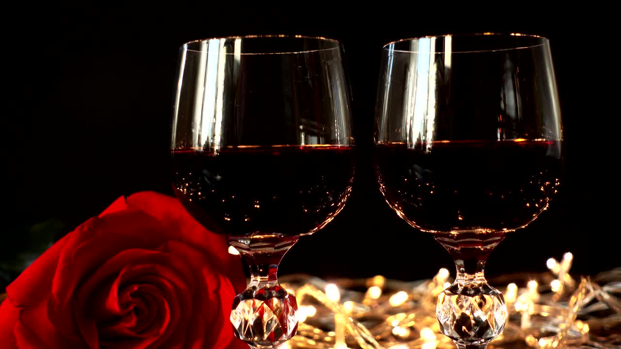 Taça com vinho e uma rosa contra o fundo de guirlandas brilhantes