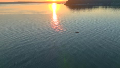 aerial drone view circling left of two people in a sea kayak paddling in a bay near seattle washington at sunrise with sun glare reflected off water