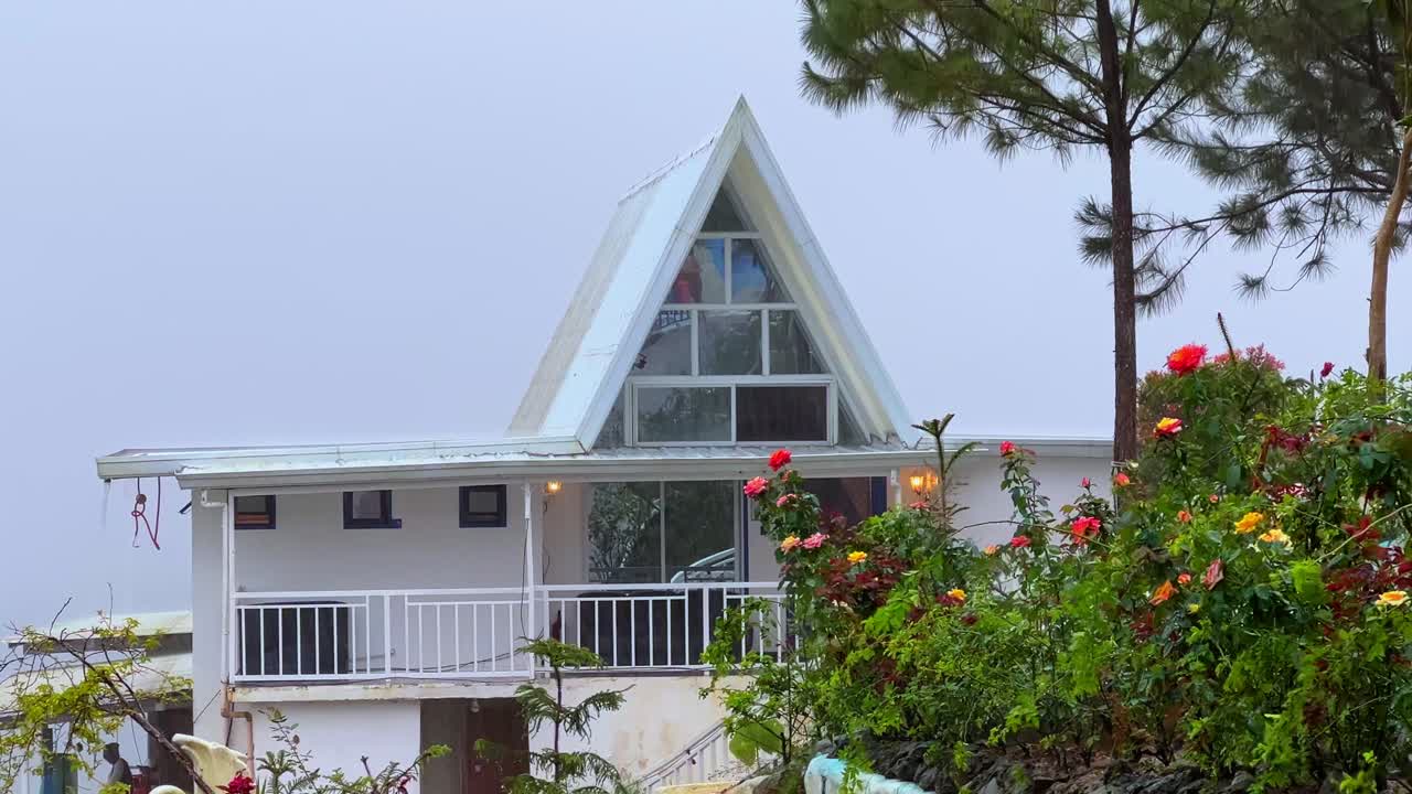 Cozy A-frame cabin in misty mountain setting, surrounded by vibrant flowers and pine trees. Ideal for travel, nature, or real estate visuals