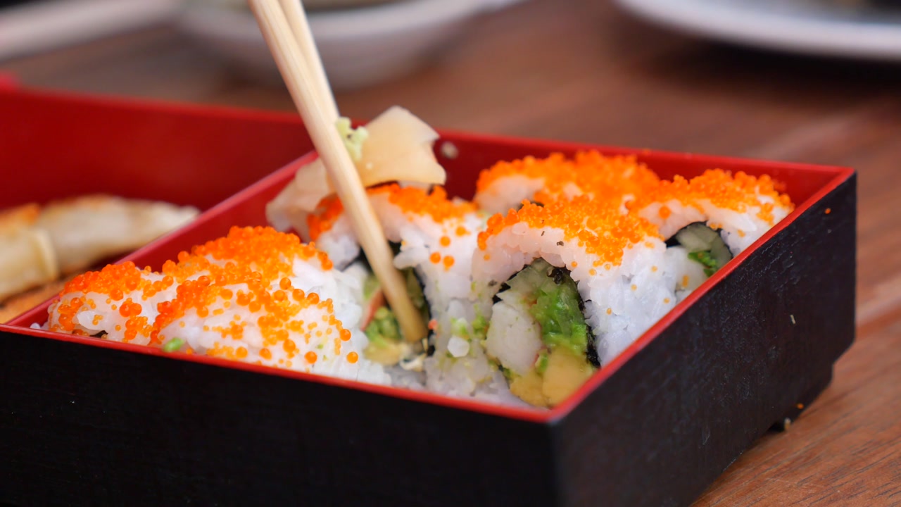 Adding Wasabi and Ginger to California Roll Sushi with Chopsticks