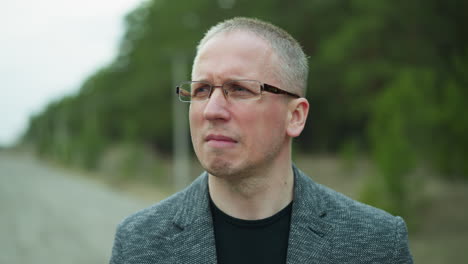 close-up view of a man in glasses and a gray jacket standing on a railway track, looking into the distance with a serious expression