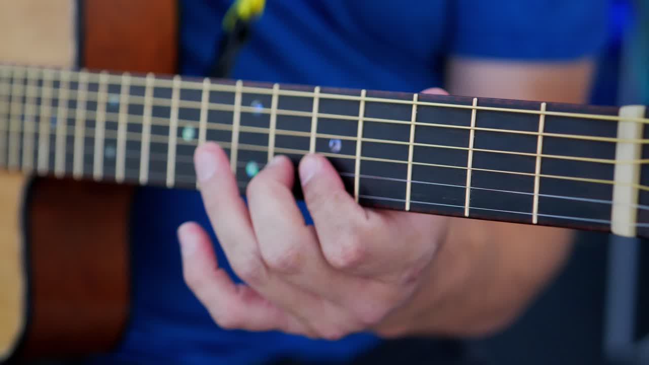 dedos de un hombre blanco caucásico con camisa azul tocando una guitarra acústica de cerca moviéndose desde la parte superior del tablero de trastes hasta la parte inferior tocando un riff solista