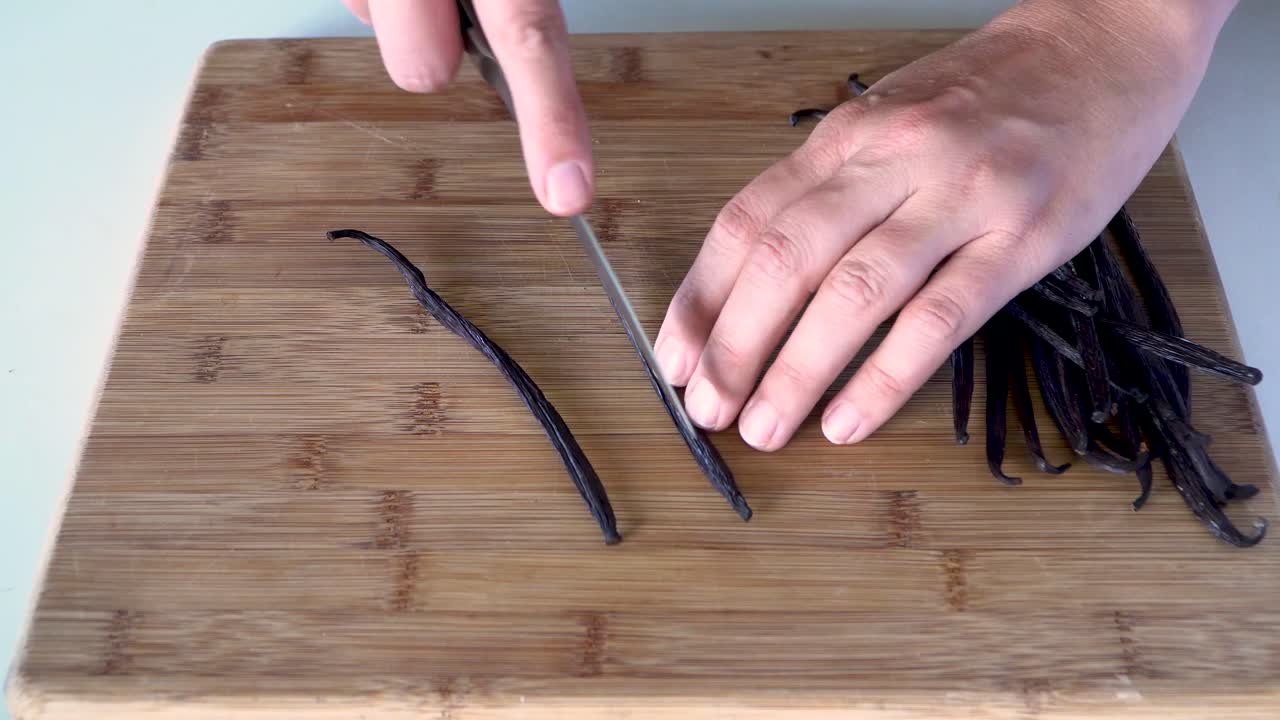 Above view hands cutting open fresh vanilla bean pods with knife