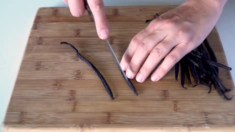 vista superior manos cortando vainas de vainilla frescas abiertas con un cuchillo