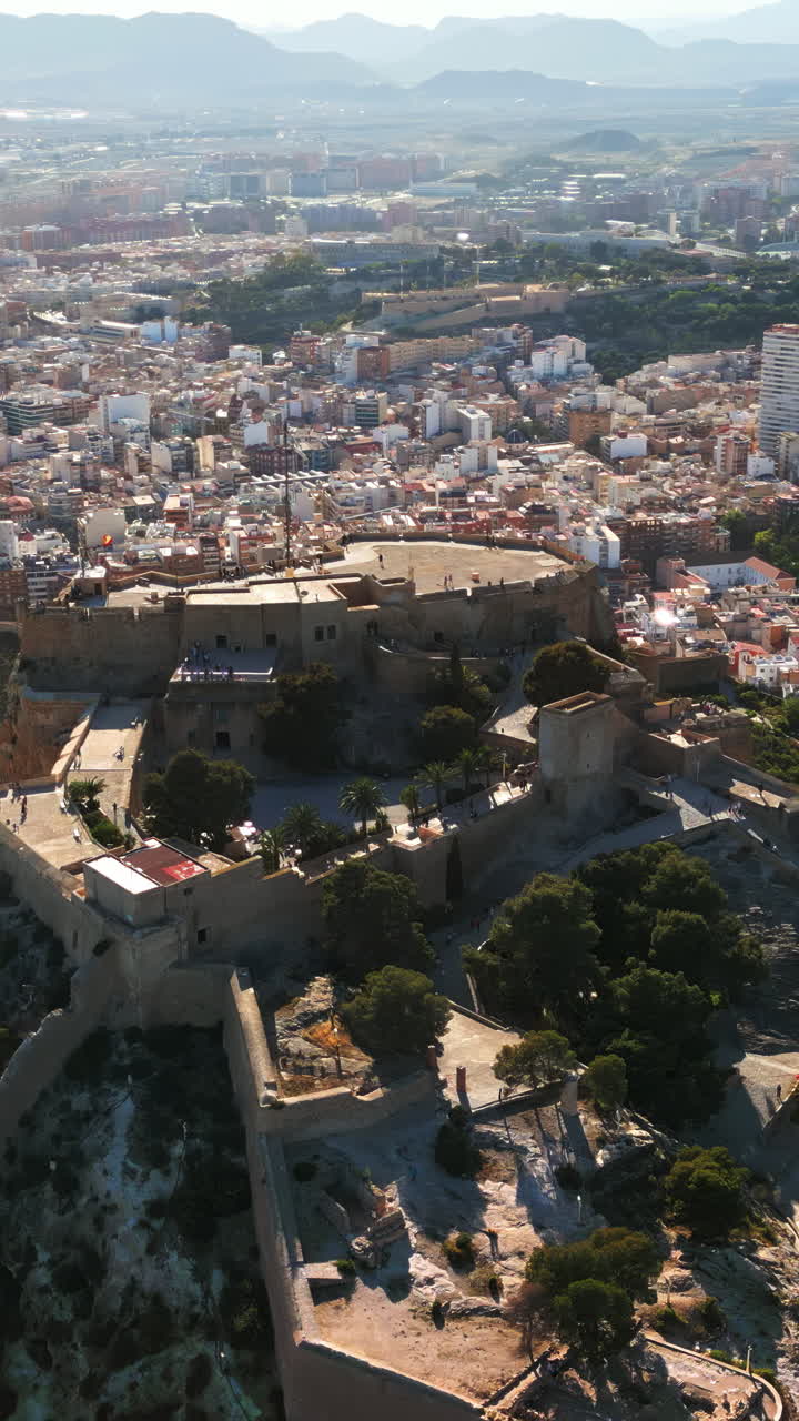 Luftdronebillede af Santa Barbara-slottet ved kysten af Alicante, Spanien, med byen i baggrunden. Lodret