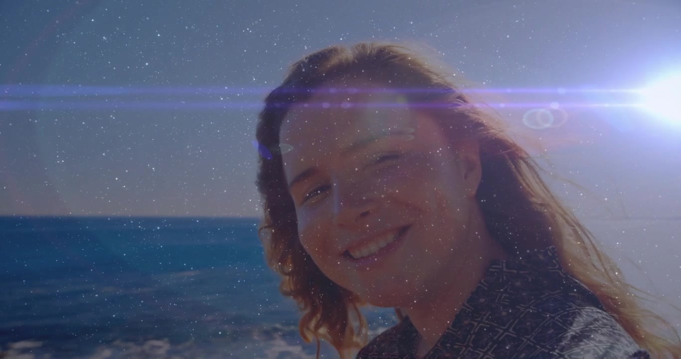 Sole che splende dietro una donna in riva all'oceano in una demo tecnologica, con bagliori dell'obiettivo che si spostano mentre la testa si gira e si svela.