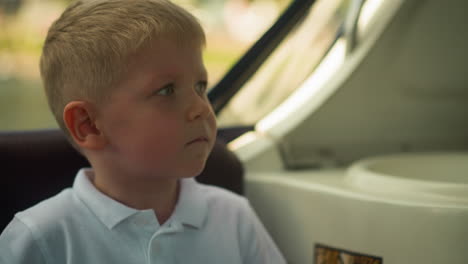 serious little boy in white polo shirt sits in motorboat cabin closeup. toddler child feels nervous while rides watercraft at resort. emotional kid