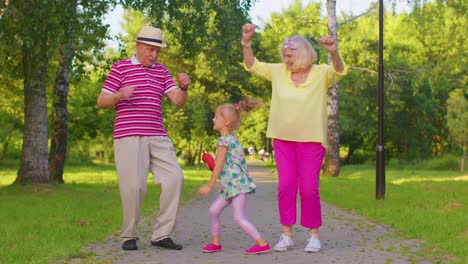 Granddaughter-together-with-senior-grandmother-grandfather-listening-to-music,-dancing-crazy-in-park