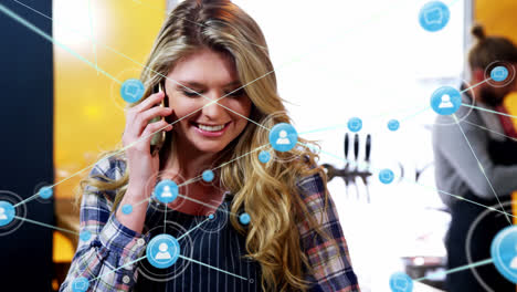 Animation-of-network-of-connections-with-icons-over-caucasian-woman-talking-on-smartphone