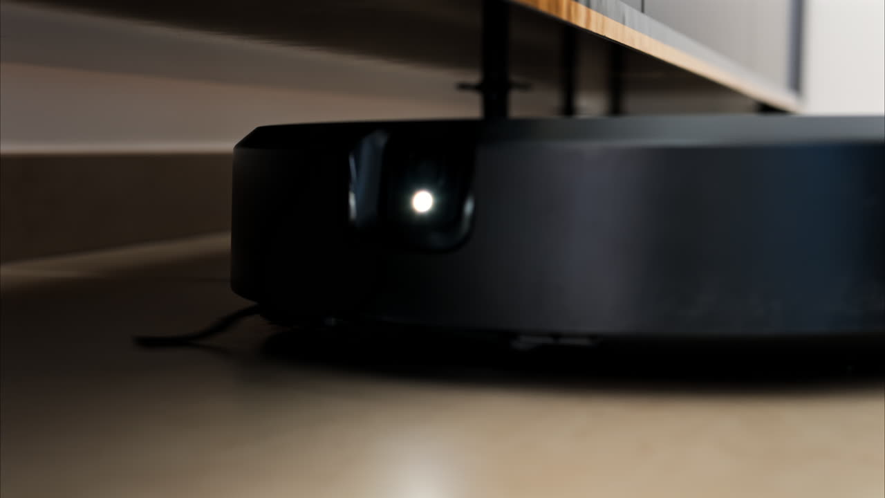 Close up of a black robot vacuum cleaner moving and rotating on the floor tiles