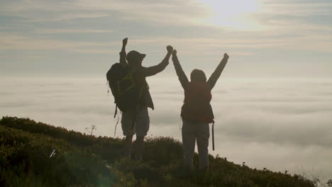 back view of happy senior hikers raising hands while standing on the top of a mountain