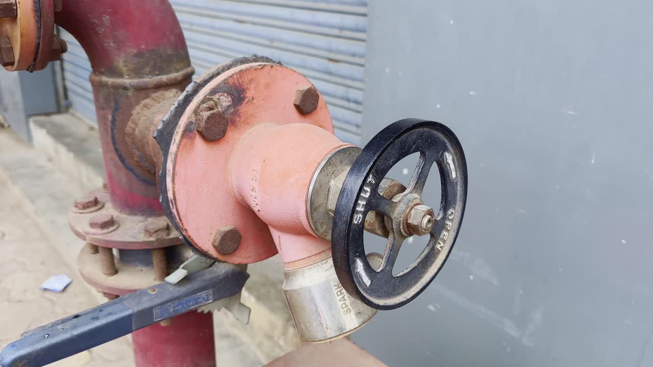 Tilt-up close shot of a fire hydrant valve with black control wheel, nuts, and metal fittings, highlighting its industrial detail