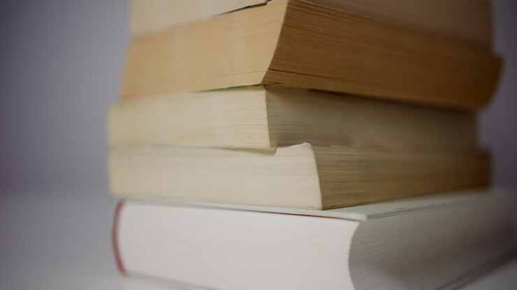 Primo piano laterale di una pila di libri ripresi con un movimento della camera molto lento da destra a sinistra, creando un concetto di calma e intramontabile di conoscenza, istruzione ed esperienza.