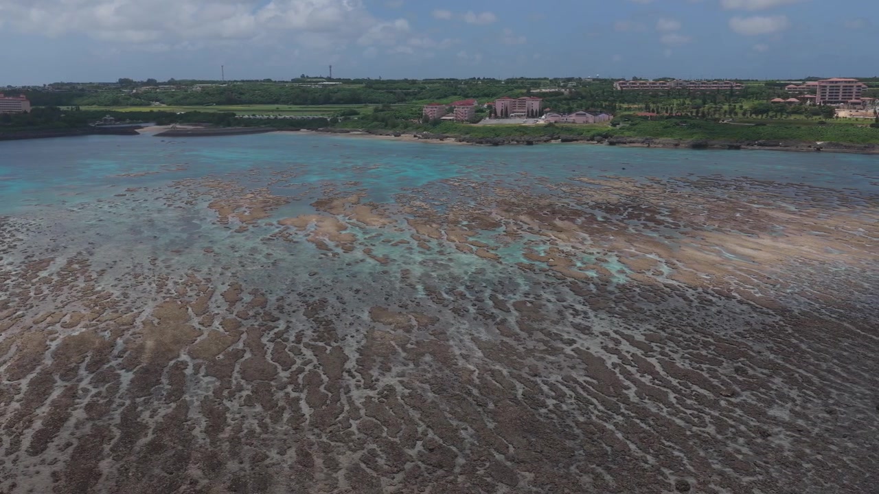Riprese aeree orizzontali che si muovono a destra sopra le piane di barriera corallina esposte e la costa di Waiwai Beach, Miyakojima, Okinawa, Giappone