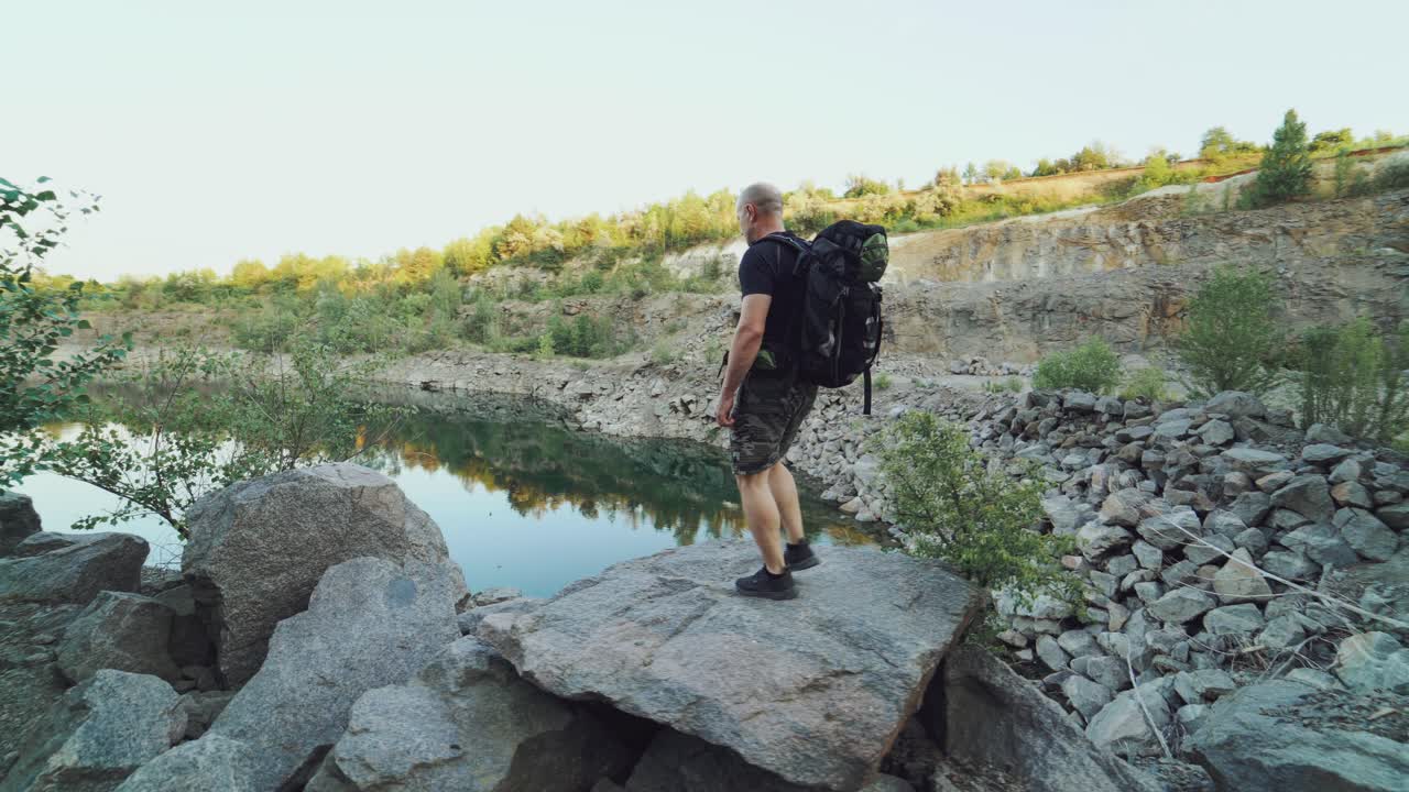 A tourist in summer clothes walks on the edge of a quarry with huge stones and looks at the beautiful lake and the nature around it. Beautiful view.