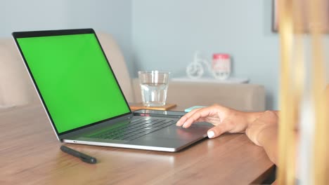 una mujer opera una computadora portátil en una mesa con pantalla verde