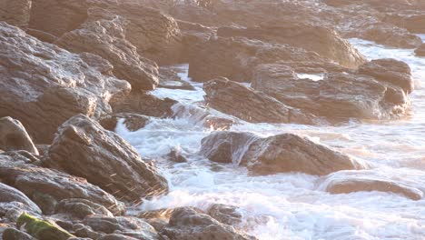 sea wave crashes on the rocks in the first rays of the sun during the huge sunrise