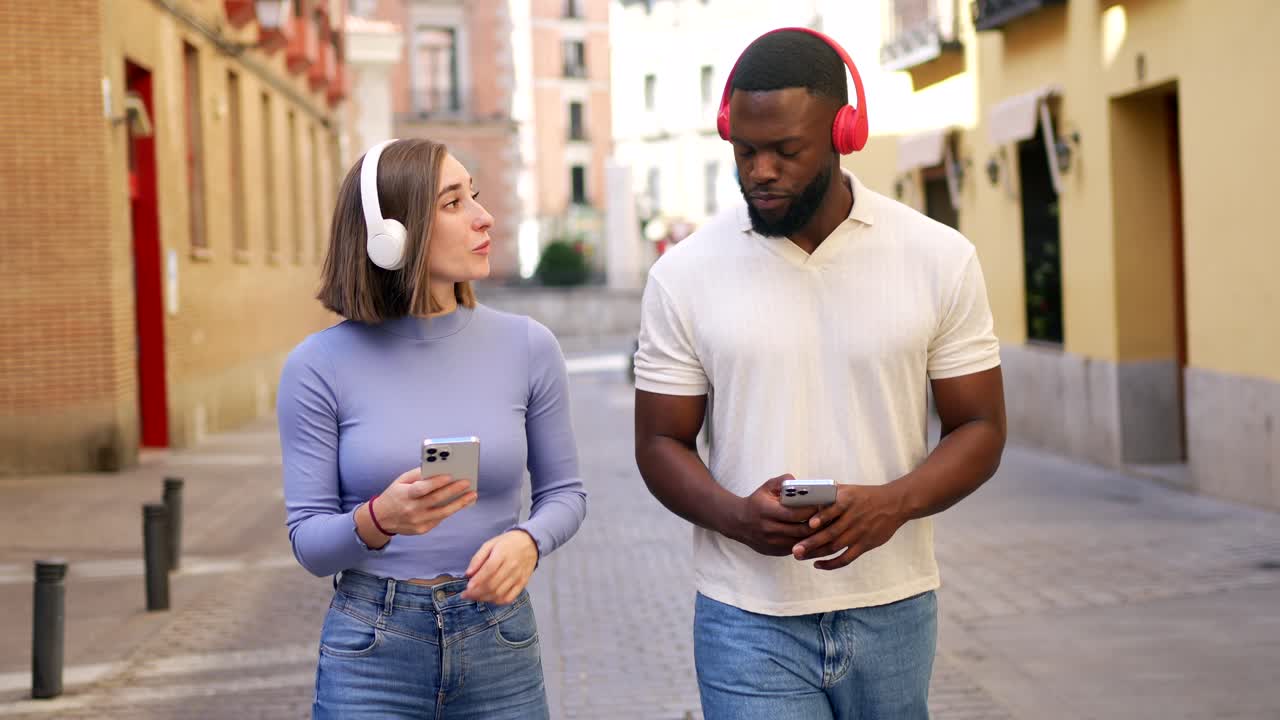 Two people walking down the street with headphones and smartphones