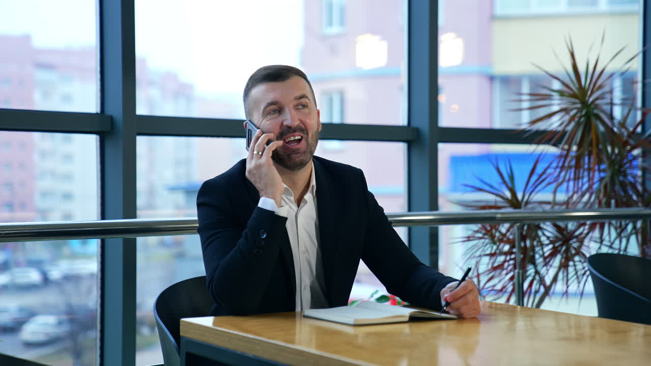 Successful businessman answering the phone in his office. Business talk in spacious light office. Business communication via smartphone.