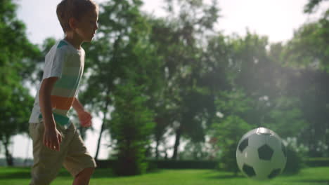 Active-boy-kick-ball-on-green-grass.-Little-sportsman-play-football-in-park.