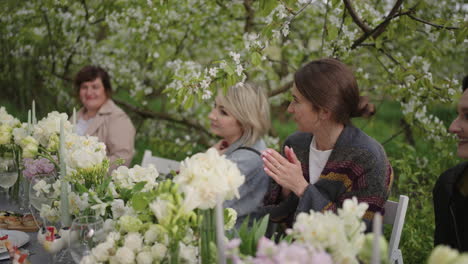 happy guests are cheering and applauding garden party in open air in blooming orchard in spring day