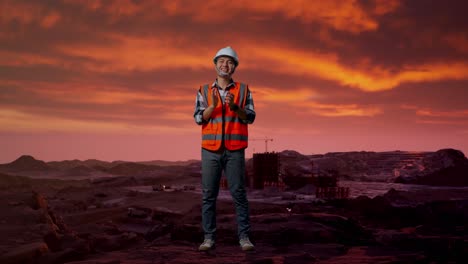 cuerpo lleno de ingeniero masculino asiático con casco de seguridad sonriendo y aplaudiendo sus manos mientras estaba de pie en el sitio de construcción, maquinaria de minería