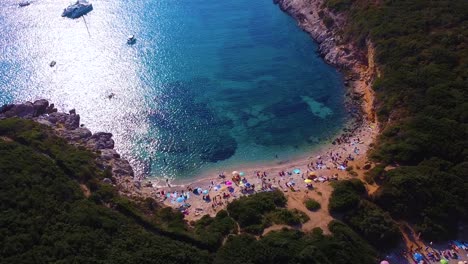 stunning drone shot of wild beach full of sunbathing people, umbrellas and floating boats