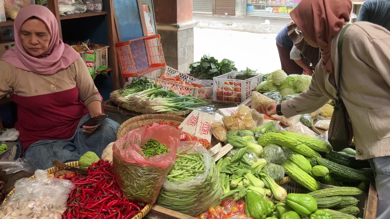 A woman wearing a hijab is buying organic vegetables sold by a vegetable trader at a traditional market.