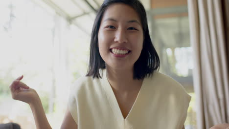 happy asian woman having video call and smiling in sunny living room, slow motion