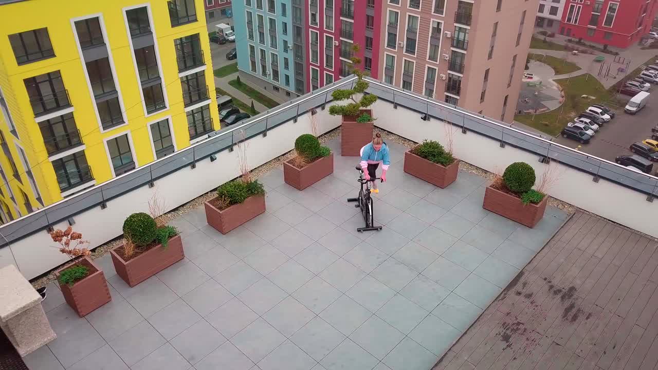 mujer blanca sana haciendo ejercicio en una máquina de ciclismo estacionaria bicicleta en el gimnasio de la azotea de la casa