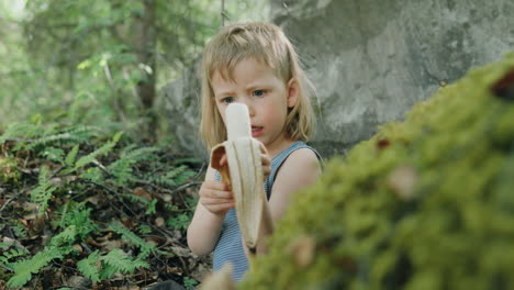 earthchild sitting outdoors in woods among lush vegetation enjoy eating a banana