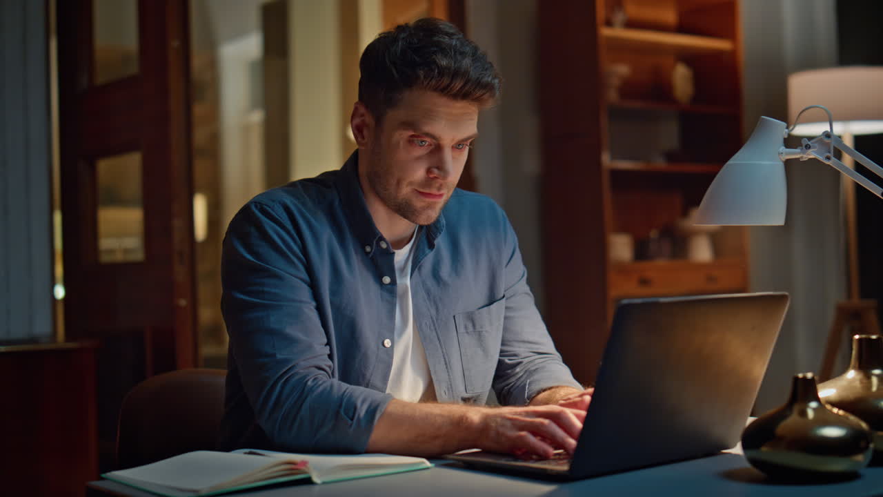 Smiling businessman browsing computer texting email at cozy dark flat closeup