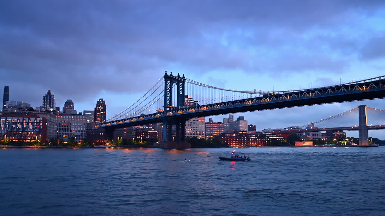 Life guard boat follows a person on canoe. Low angle view on the Manhattan Bridge and New York skyline at dusk time