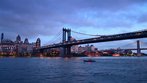 life guard boat follows a person on canoe. low angle view on the manhattan bridge and new york skyline at dusk time