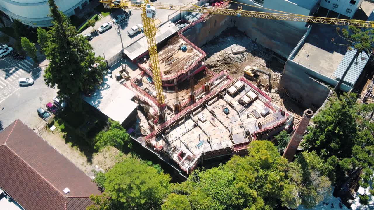 timelapse aéreo de un sitio de construcción de edificios con albañiles, una excavadora y una grúa