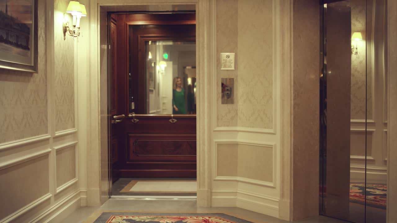 Ascensore vuoto che si apre nel corridoio di un hotel di lusso. Una donna che entra nella cabina dell'ascensore.