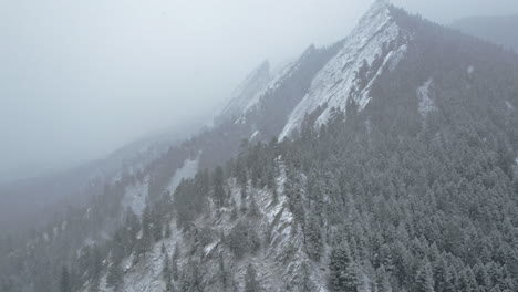 drone aerial footage flying back from pine tree snowcapped flatirons mountain near boulder colorado usa during snowstorm blizzard