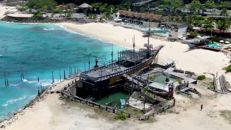 beautiful ancient wooden ship moored near luxury resorts of bali, aerial orbit view