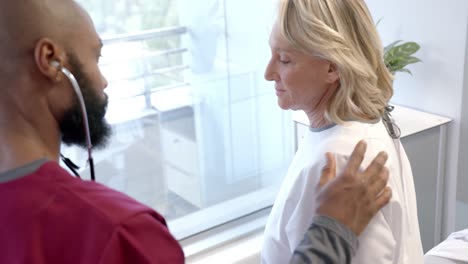 African-american-male-doctor-with-stethoscope-examining-caucasian-female-patient-at-hospital