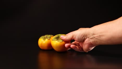 una mano mueve persimones en una superficie oscura