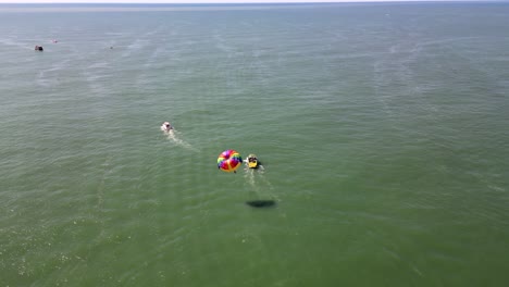 aerial drone footage captures vibrant parasailing on the green black sea near batumi, georgia. a colorful boat tows a parachutist, showcasing summer joy and scenic horizons.