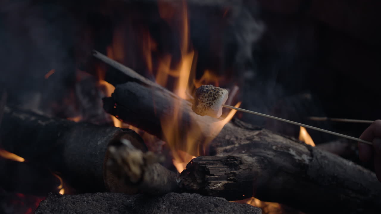Roasting marshmallows in campfire with radiant embers beneath (closeup shot)