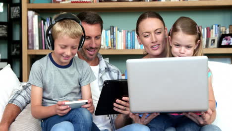 Linda-Familia-Usando-Tecnologías-Sentadas-En-El-Sofá