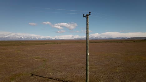 Luftaufnahmen,-Vorbei-An-Einem-Hölzernen-Strommast-In-Einer-Weiten,-Trockenen-Landschaft-Mit-Bergen-Im-Hintergrund