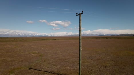 imágenes aéreas, pasando cerca de un poste de energía de madera en un paisaje vasto y seco con montañas en el fondo